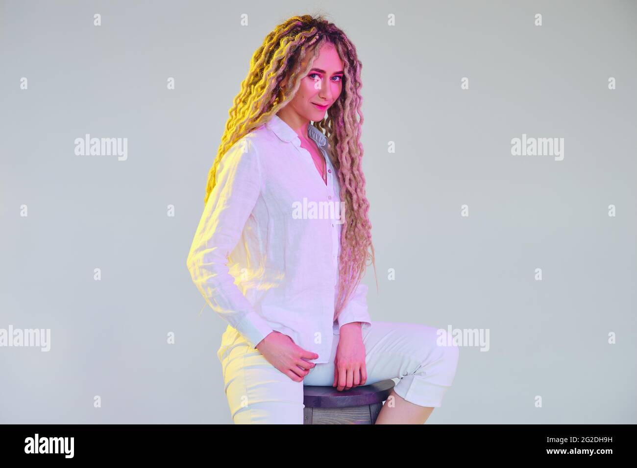 Knifflige Frau in weißer Bluse und Hose unter Neonlicht Stockfoto