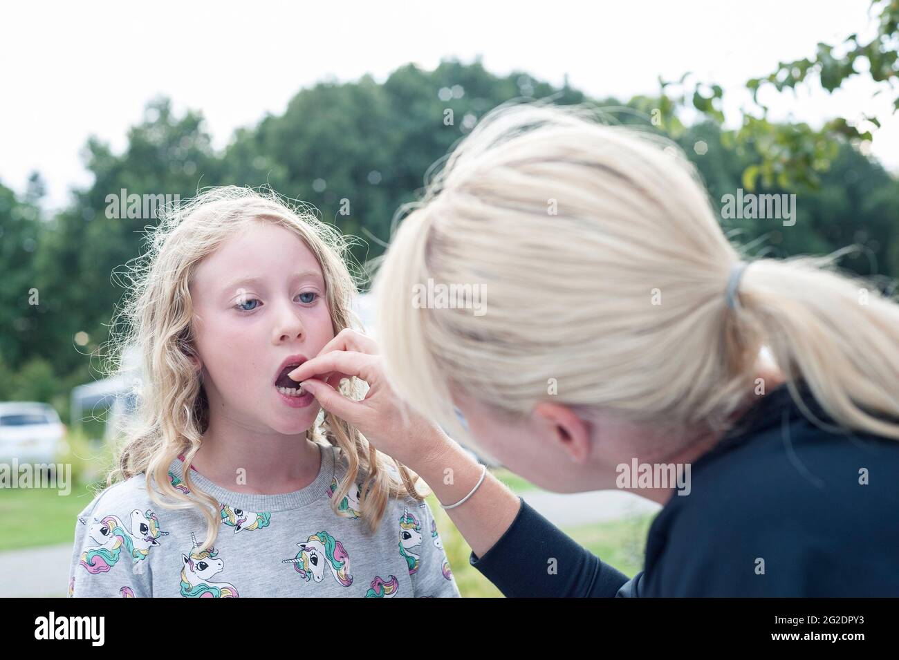 Ein junges Mädchen hat ihren ersten Zahn von ihrer Mutter herausgezogen. Stockfoto