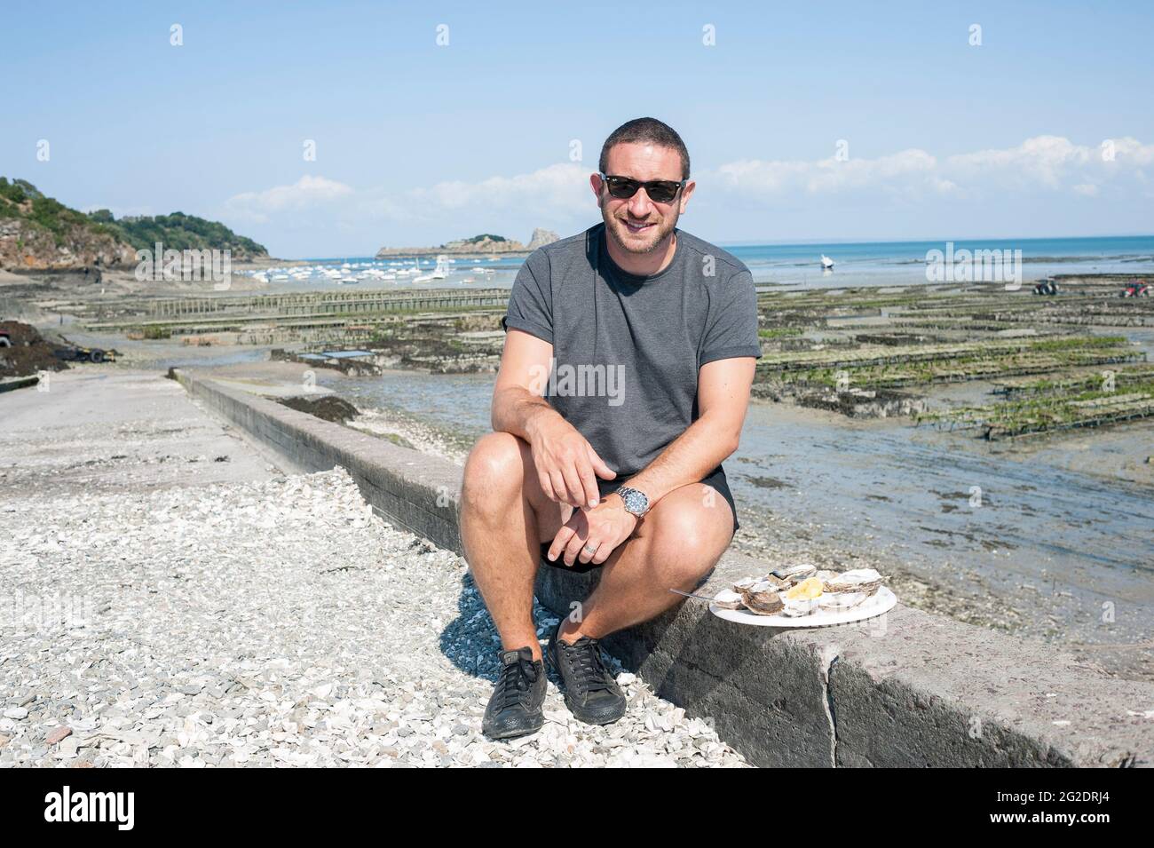 Eine Person, die Austern frisch aus den Austernbeeten am Meer im französischen Dorf Cancale in der Bretagne an der Nordküste Frankreichs probiert. Stockfoto