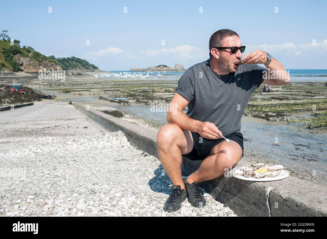 Eine Person, die Austern frisch aus den Austernbeeten am Meer im französischen Dorf Cancale in der Bretagne an der Nordküste Frankreichs probiert. Stockfoto