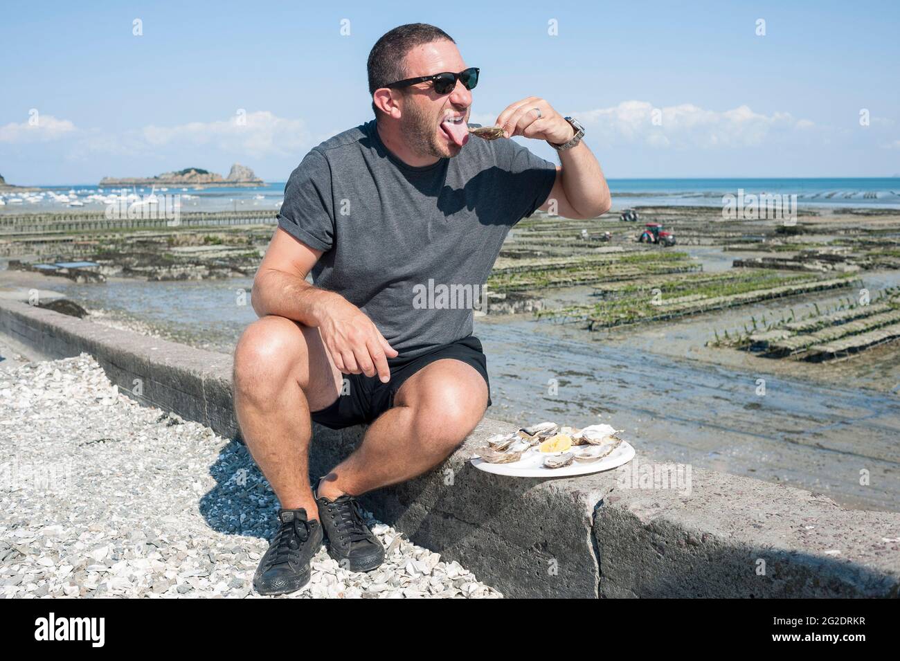 Eine Person, die Austern frisch aus den Austernbeeten am Meer im französischen Dorf Cancale in der Bretagne an der Nordküste Frankreichs probiert. Stockfoto