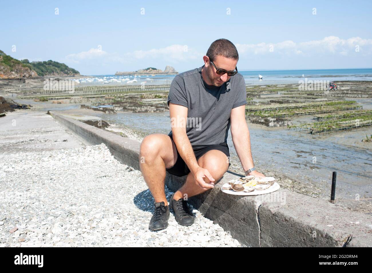 Eine Person, die Austern frisch aus den Austernbeeten am Meer im französischen Dorf Cancale in der Bretagne an der Nordküste Frankreichs probiert. Stockfoto