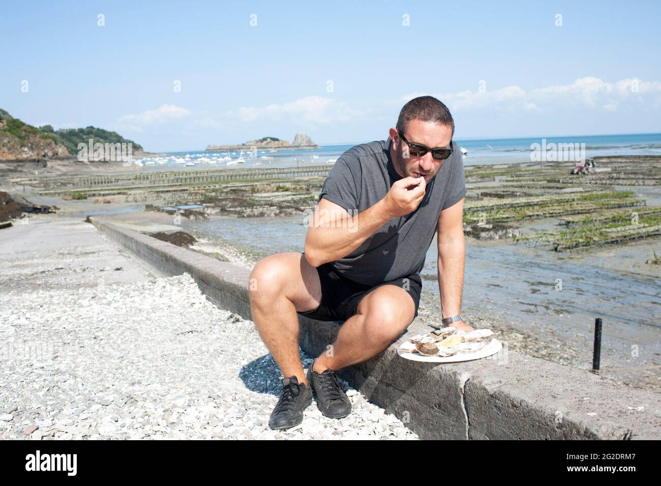 Eine Person, die Austern frisch aus den Austernbeeten am Meer im französischen Dorf Cancale in der Bretagne an der Nordküste Frankreichs probiert. Stockfoto