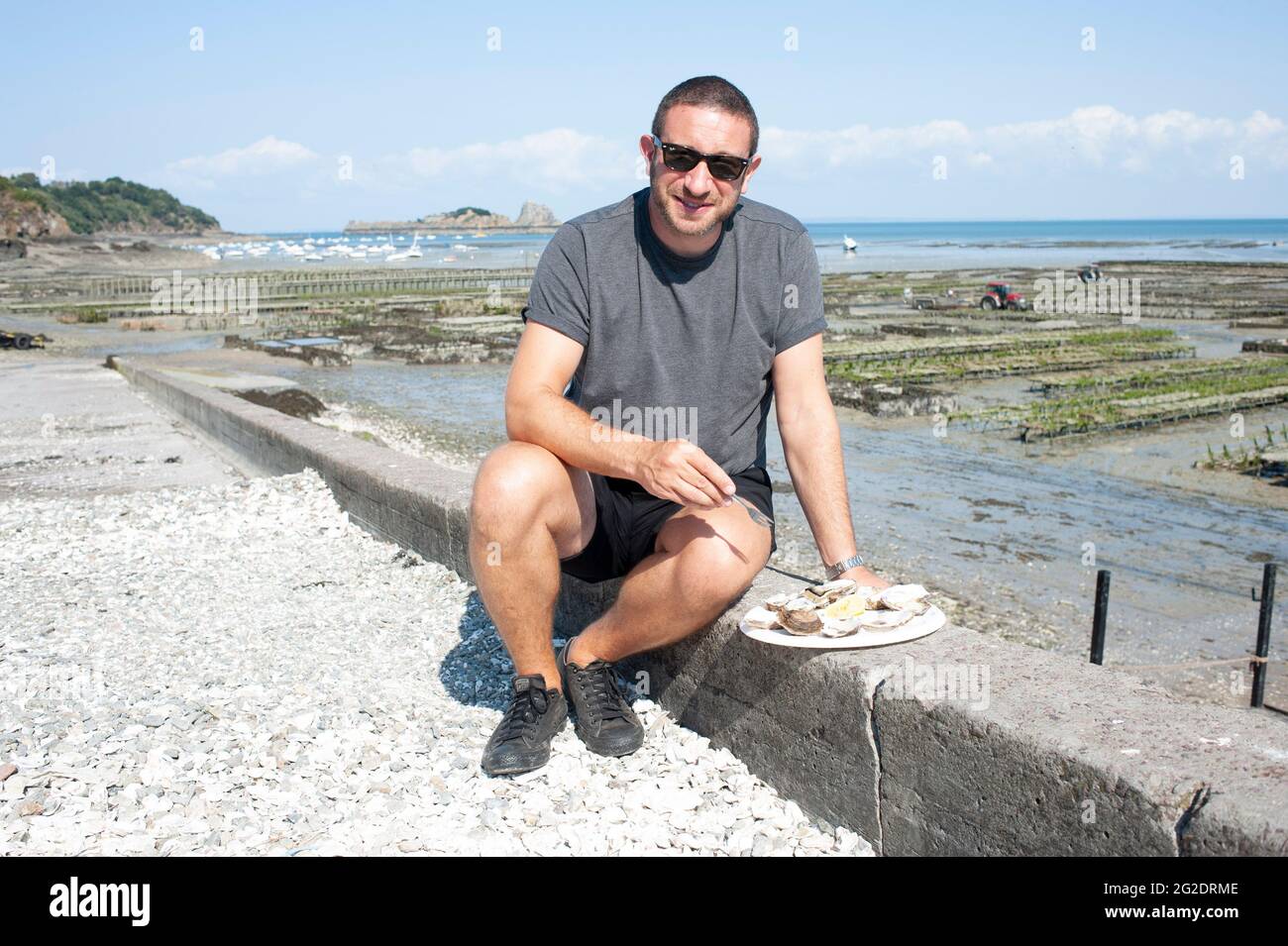 Eine Person, die Austern frisch aus den Austernbeeten am Meer im französischen Dorf Cancale in der Bretagne an der Nordküste Frankreichs probiert. Stockfoto