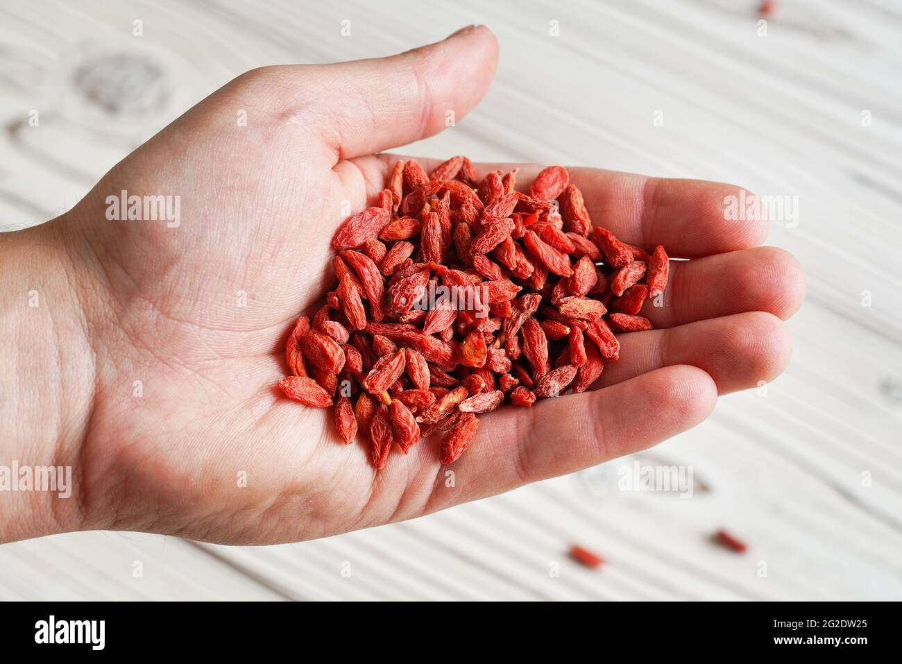 Junger Mann mit getrockneten Goji-Beeren über dem Schreibtisch mit weißen Brettern, Details aus der Nähe Stockfoto