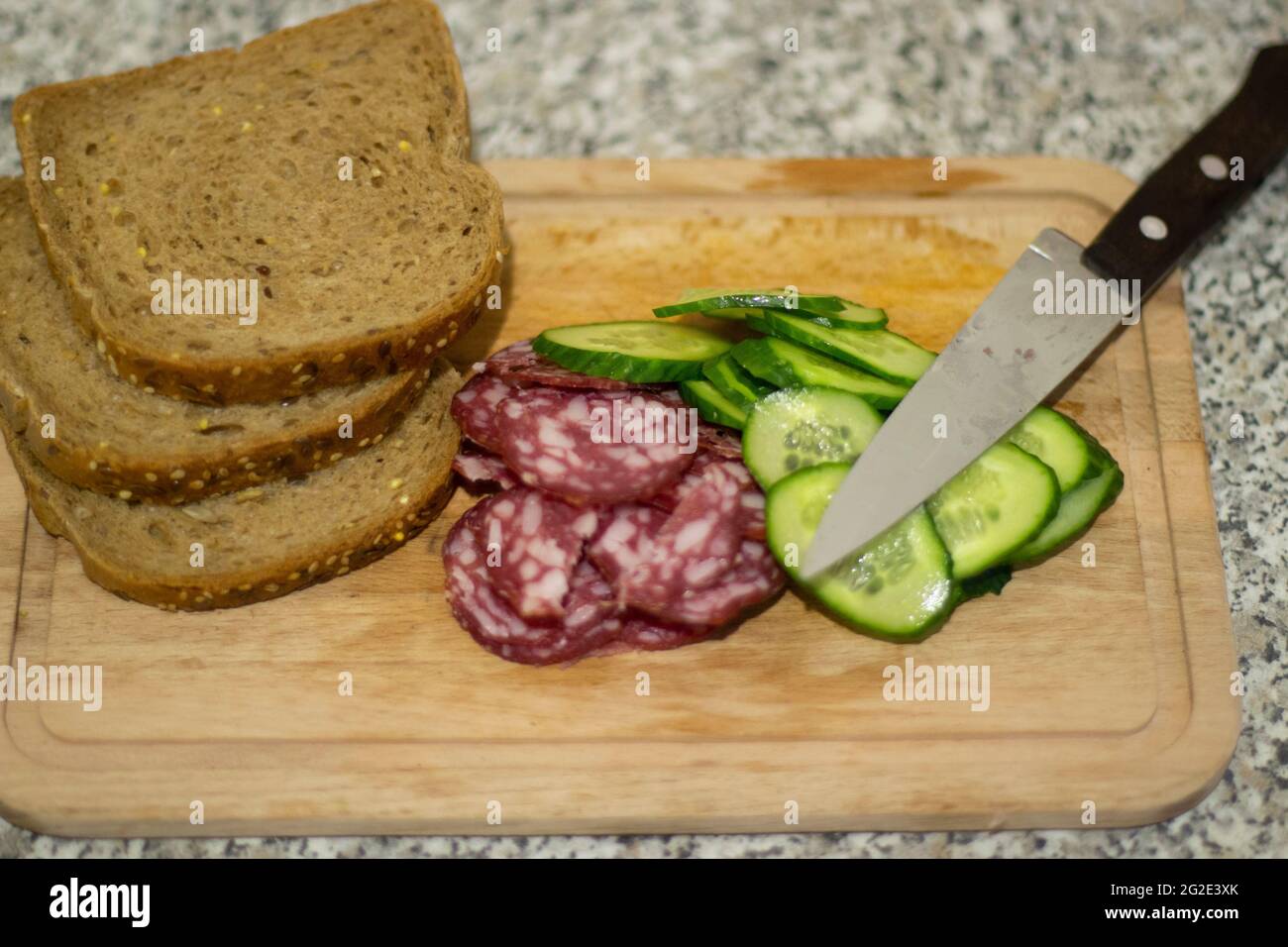 Ein Wurstsandwich. Frühstück mit Brot und Gurke. Wurst auf einem Brett geschnitten. Einfaches Essen aus Zutaten. Stockfoto