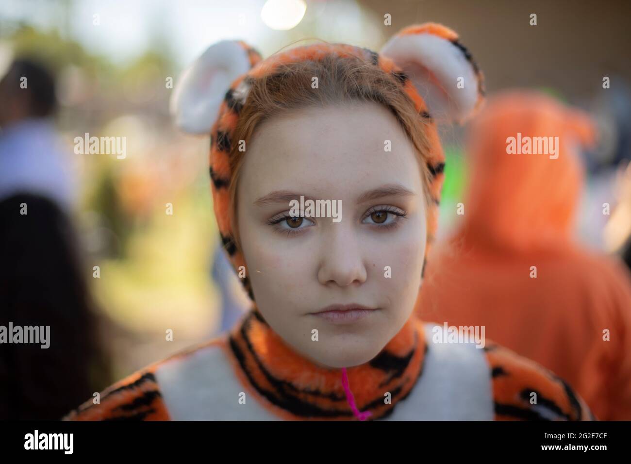 Ein Mädchen, das als Tiger gekleidet ist. Kinder-Animotr in einem weichen Kostüm einer wilden Katze. Ein nettes Mädchen mit roten Haaren in einem fröhlichen Outfit gekleidet. Stockfoto