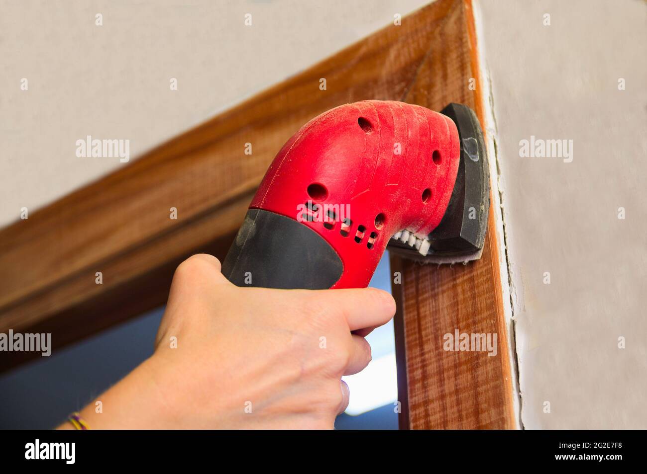 Eine Frau verwendet eine elektrische Schleifmaschine, um das Holz eines Türrahmens zu lackieren Stockfoto