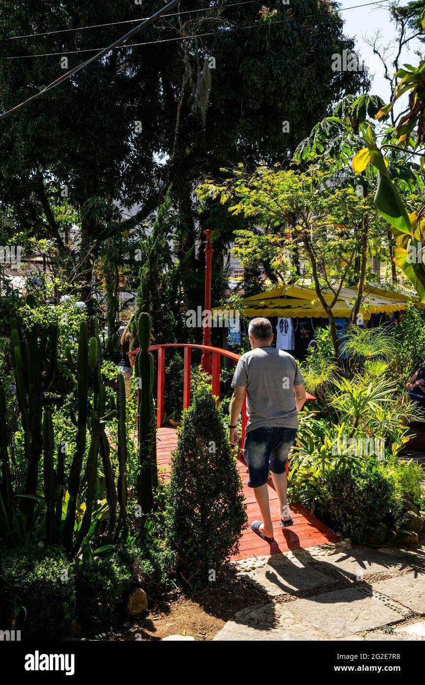 Ein alter Mann, der an einem sonnigen Tag zwischen den Gärten des Platzes Higino da Silveira auf eine schmale Brücke geht, im Viertel Alto. Stockfoto