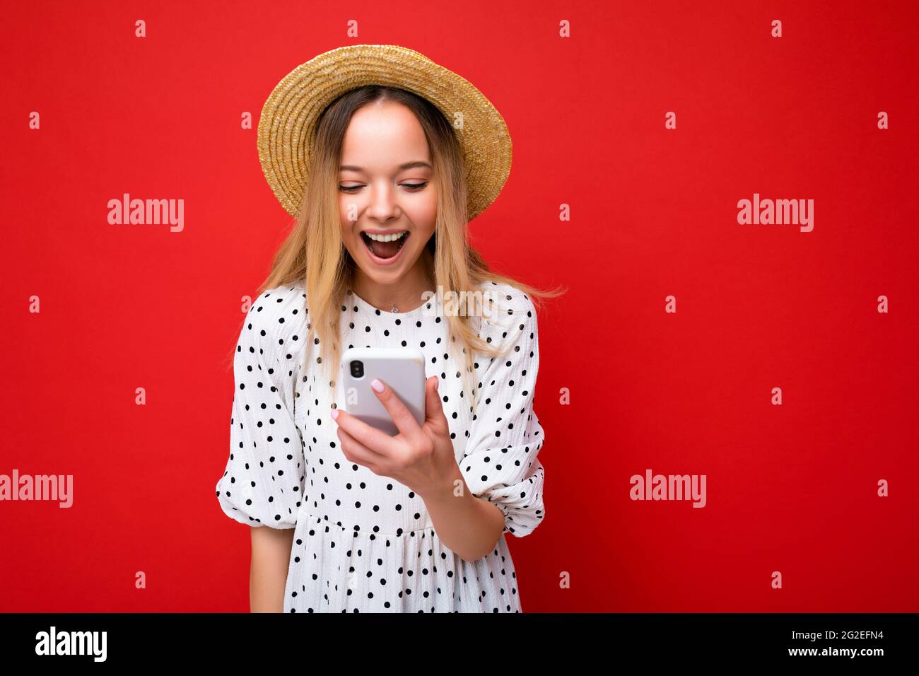 Schöne, überraschte junge Frau in lässiger Kleidung, die isoliert im Hintergrund über das Internet per Telefon auf dem mobilen Bildschirm schaut, surft Stockfoto