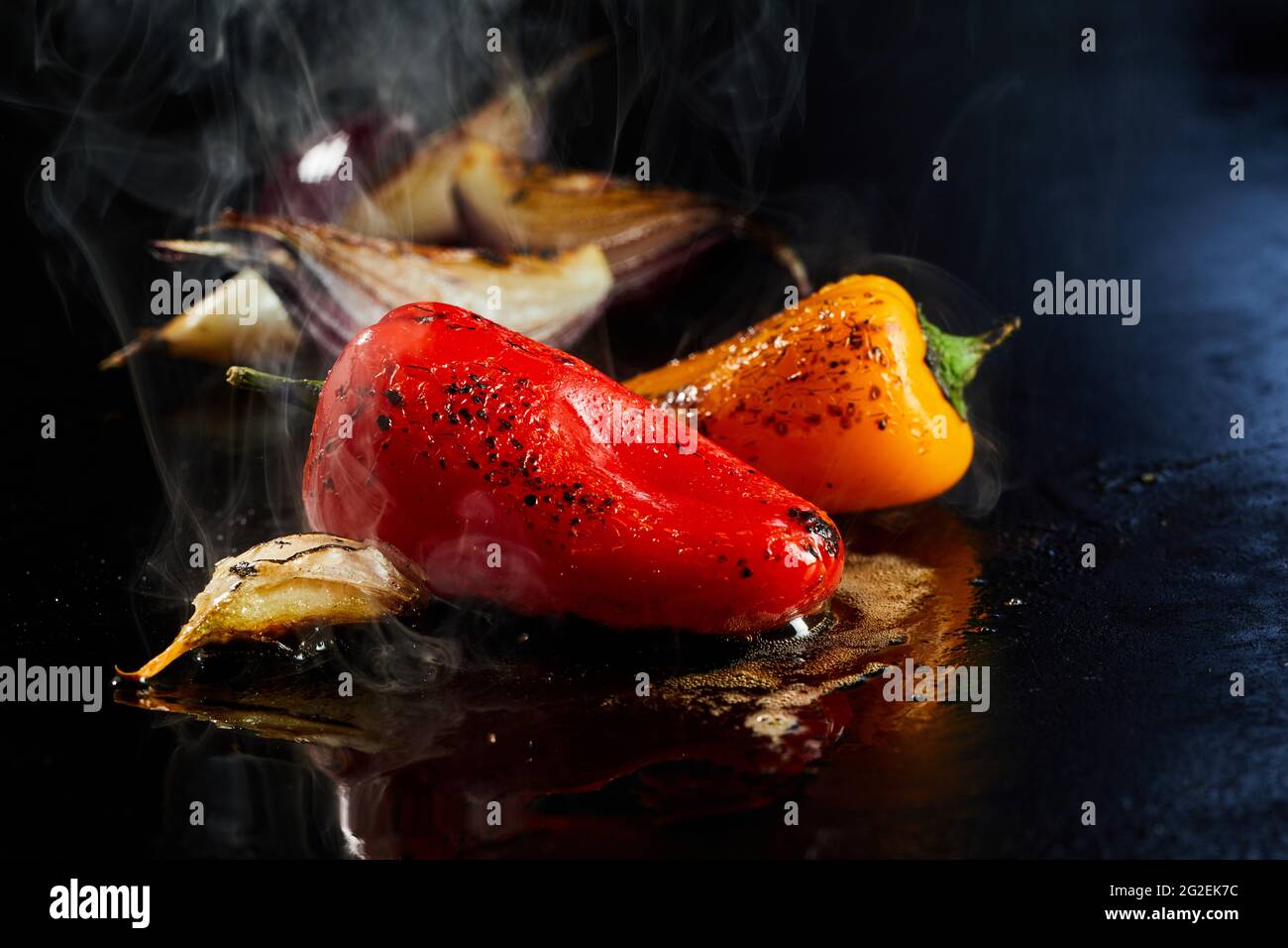 Appetitliche Paprika Zubereitung mit Knoblauch und Zwiebel auf schwarzer, heißer Oberfläche in Öl Stockfoto
