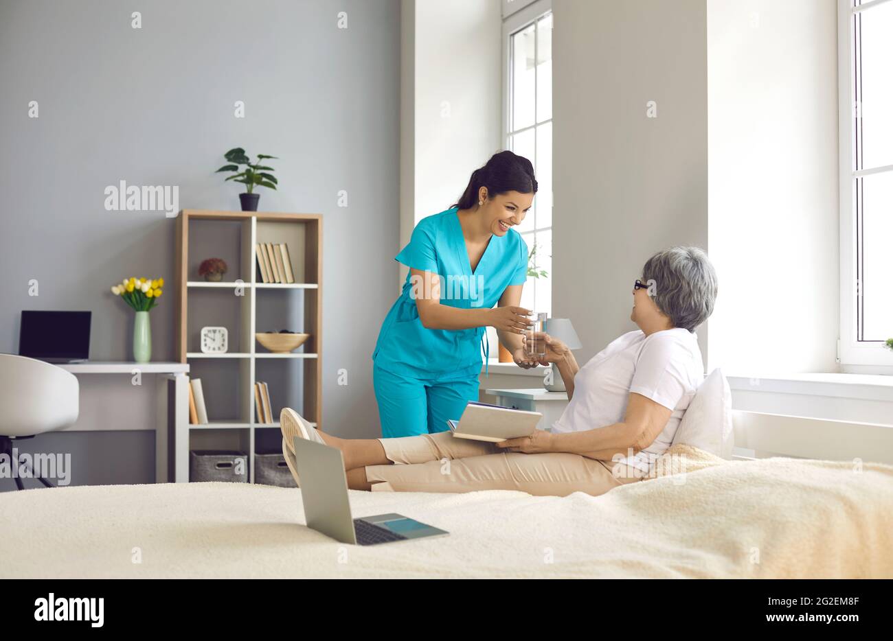 Krankenschwester, die der alten Patientin, die auf dem Bett liegt, Glas mit Wasser gab Stockfoto Krankenschwester, die der alten Patientin, die auf dem Bett liegt, Glas mit Wasser gab Stockfoto