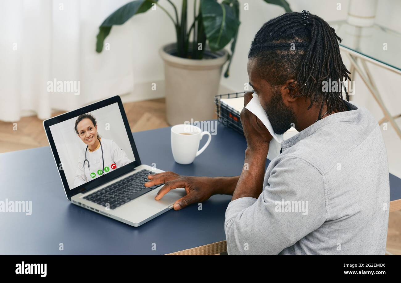 Ein erwachsener Mann mit Taschentuch hält von zu Hause aus eine medizinische Online-Konferenz mit seinem Hausarzt zur Behandlung seiner Krankheit ab Stockfoto