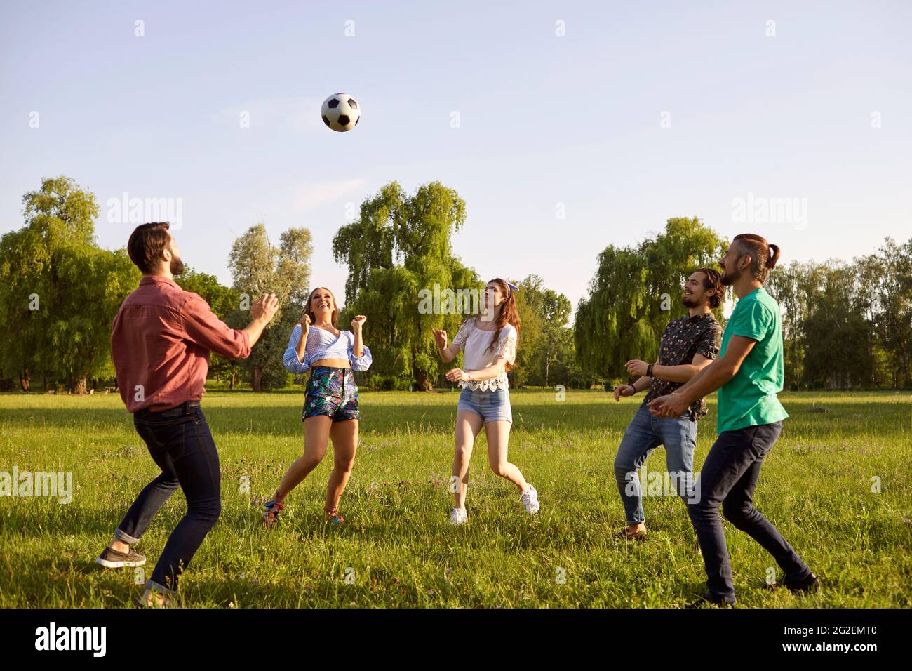 Fröhliche Freunde spielen mit einem Ball auf dem Rasen in einem Sommerpark. Stockfoto