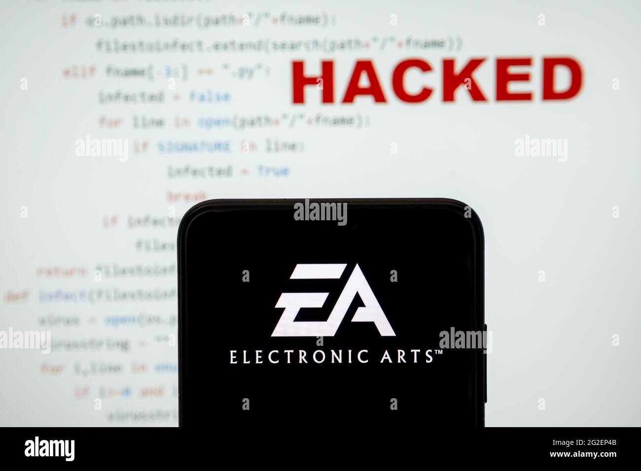 EA Electronic Arts-Logo auf einer Silhouette des Smartphones und einfacher Quellcode auf mit Wort GEHACKT auf verschwommenem Hintergrund. Konzept. ECHTES FOTO, Stockfoto
