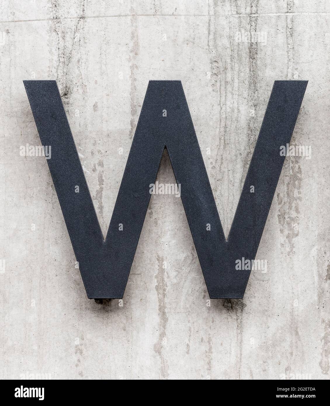 Anthrazitgrauer Metallbuchstabe W auf Betonwand Stockfoto