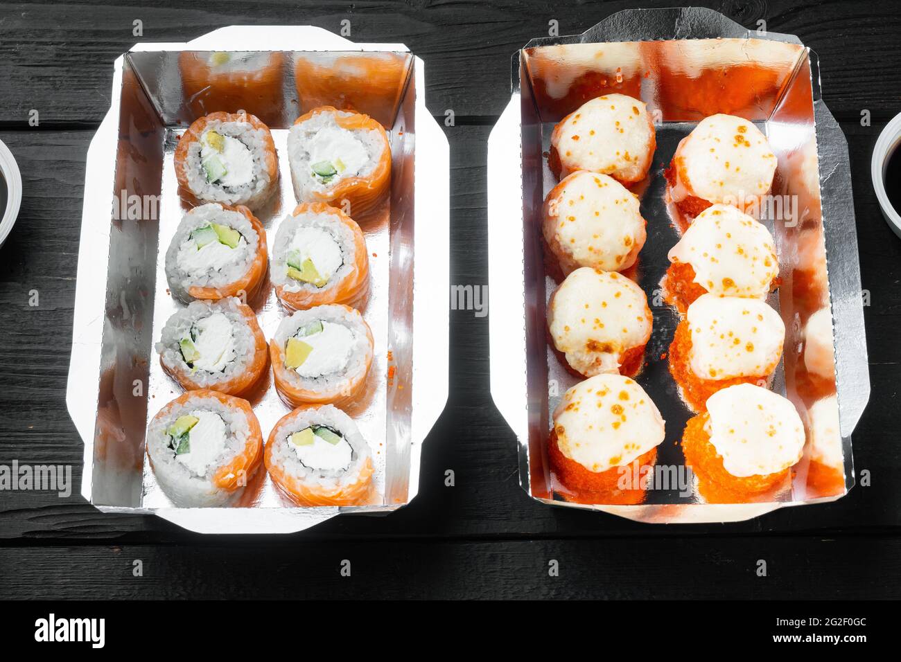 Set von Sushi-Rollen im Lieferkarton-Set, auf schwarzem Holztisch-Hintergrund Stockfoto