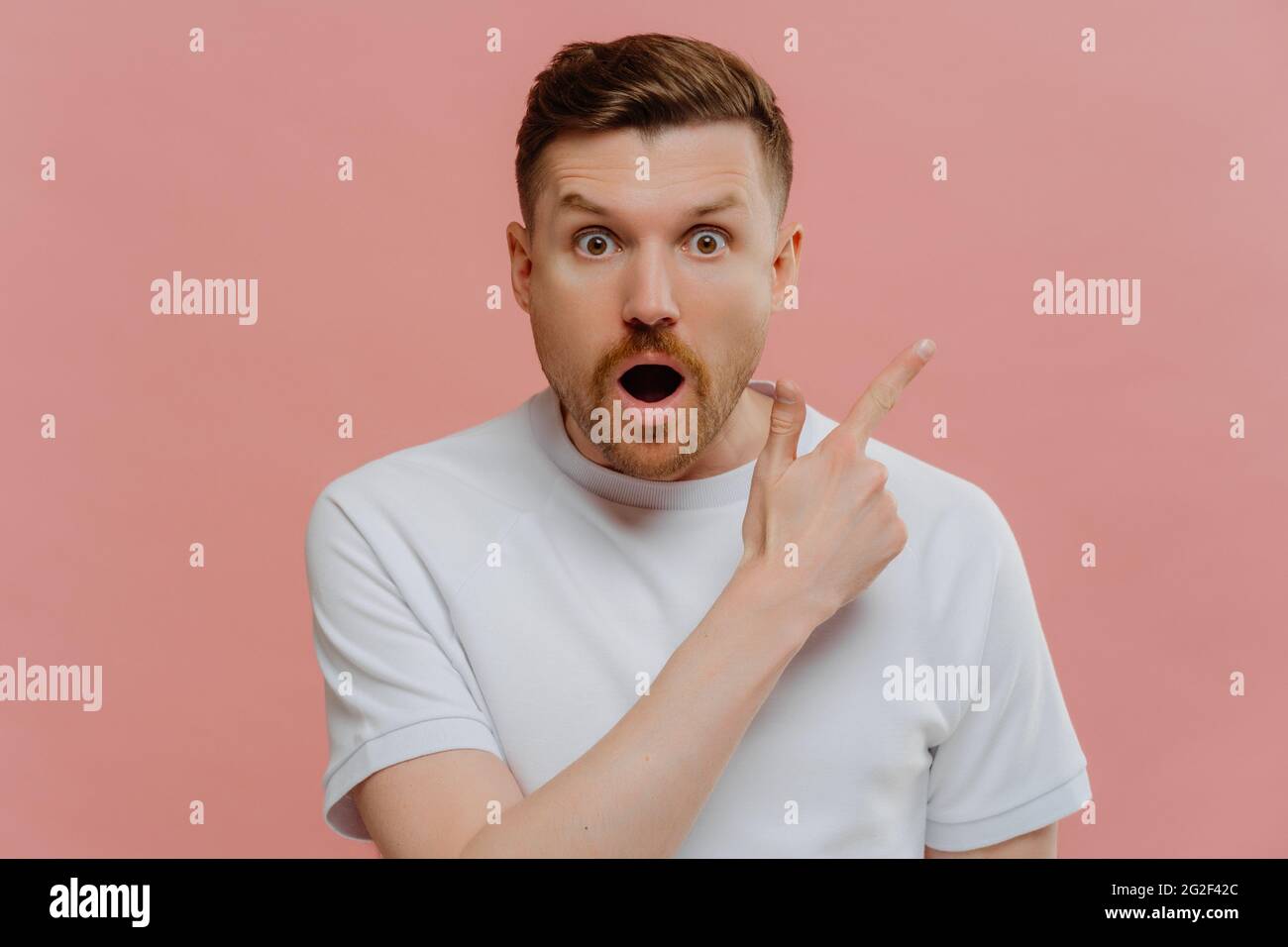 Schockierter junger Mann, der mit einem Finger zur anderen zeigt und einen überraschten Gesichtsausdruck zeigt Stockfoto