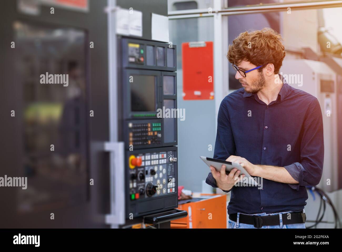 Junger amerikanischer Ingenieur Arbeiter, der schwere industrielle Maschine in der Fabrik programmiert. Angestellte, der CNC-Maschine in der Produktionslinie schaut und steuert. Stockfoto