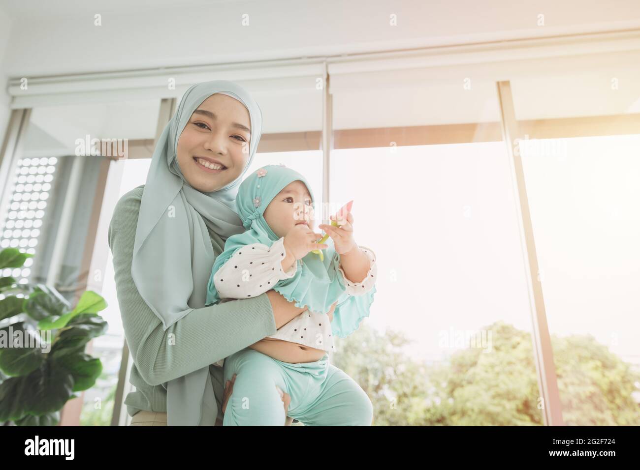 Muslim Hijab hält ihr Kind Baby glücklich lächeln zu Hause. Mutter Pflege gesunde Säugling aussehende Kamera. Stockfoto