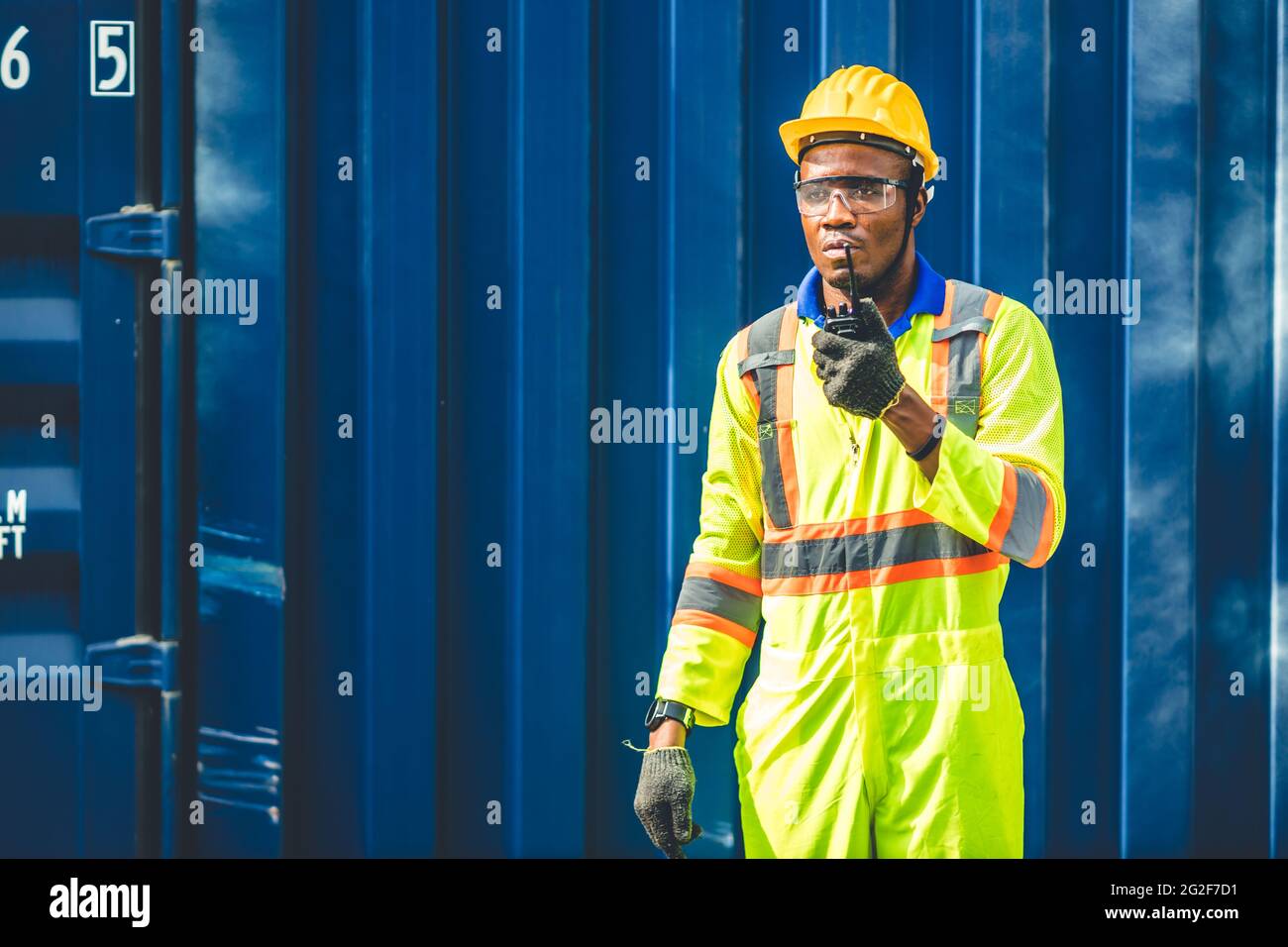 Schwarzer afrikanischer Arbeiter, der in der logistischen Schifffahrt Radio-Kontrolle Befehl Laden von Containern am Schifffahrtshafen arbeitet. Personal Fracht für Import Exportgüter Stockfoto