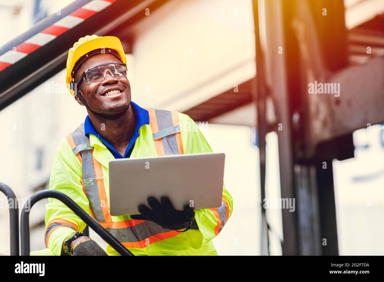 Schwarzer afrikanischer glücklicher Arbeiter, der in der logistischen Schifffahrt mit Laptop-Computersteuerung arbeitet, um Container auf Hafenfracht zu laden. Import Export Schifffahrt Industrie Stockfoto