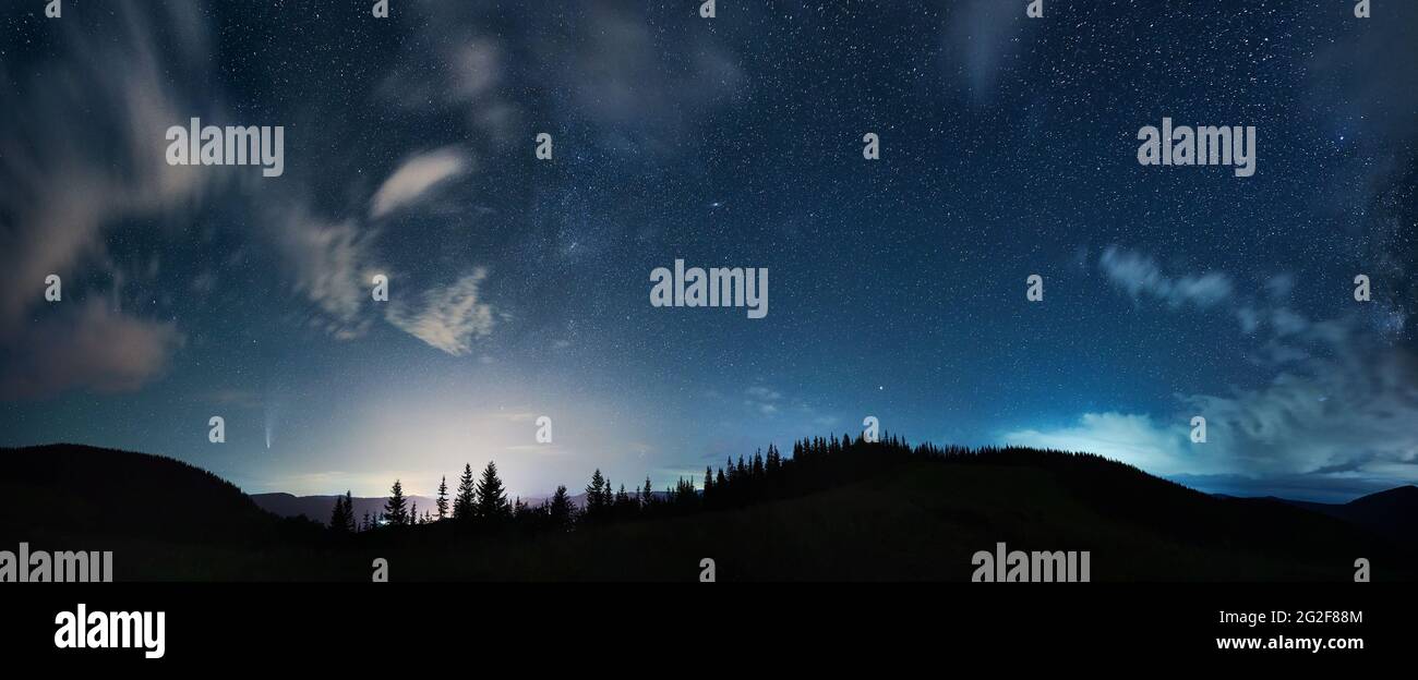 Herrlicher Panoramablick auf den nächtlichen Sternenhimmel über Nadelwald in den Bergen. Fantastische Landschaft von Bergwald mit Nadelbäumen unter blauem Himmel mit Sternen. Konzept der Nacht und Galaxie. Stockfoto