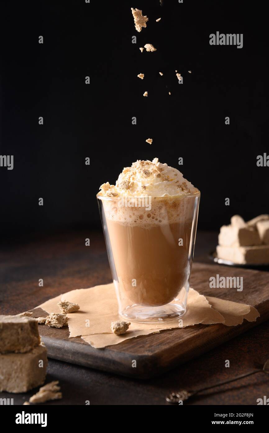 Streut halawa in trendiger Rezeptur Kaffee Latte mit Halva in moderner Glasschale auf dunkelbraunem Hintergrund. Vertikal. Nahaufnahme. Stockfoto