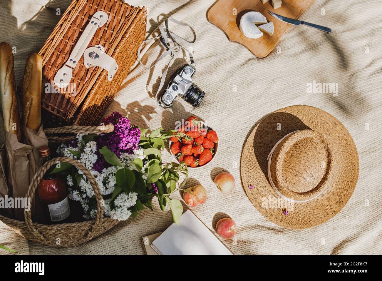 Sommerpicknick mit Essen und Trinken in Weidenkorb, Buch und weiblichem Strohhut. Stockfoto