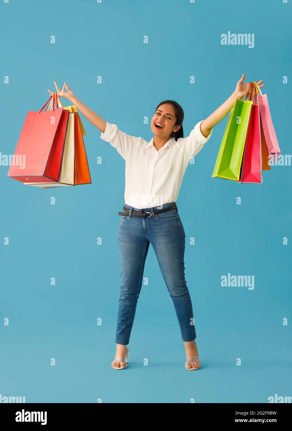 EINE GLÜCKLICHE JUNGE FRAU, DIE SPIELERISCH DIE ARME MIT EINKAUFSTASCHEN HOCHHEBT Stockfoto