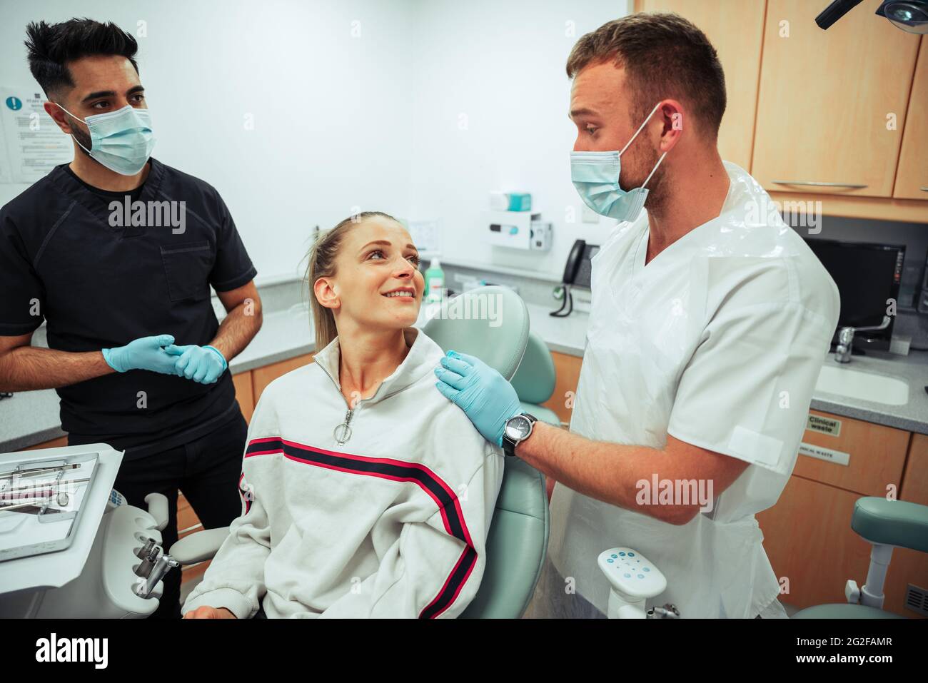 Kaukasisch lächelnde Frau, die auf dem Ärztebett liegt, während sie sich mit männlichen Krankenschwestern im Arztbüro unterhält Stockfoto