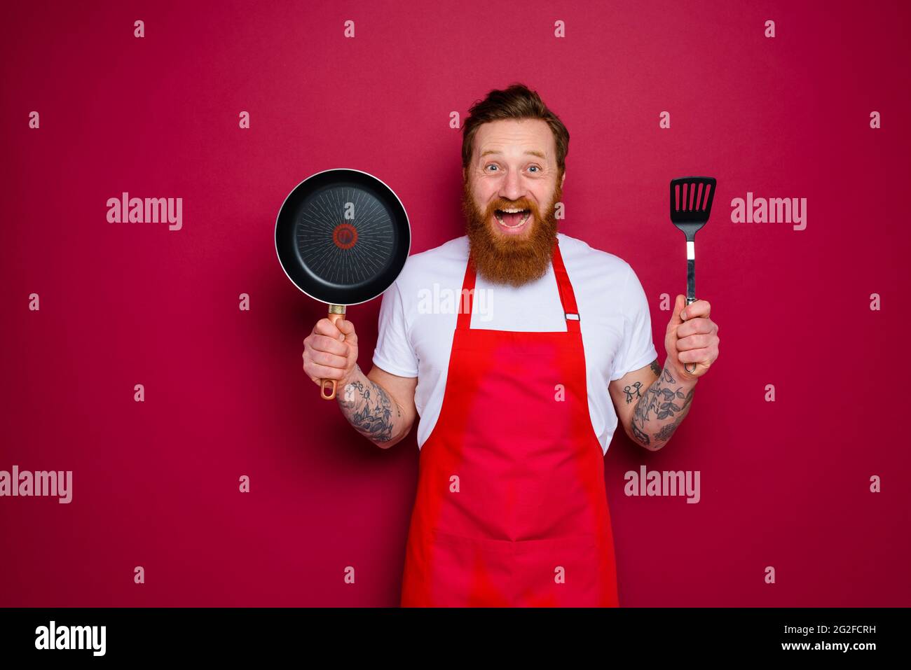 Der glückliche Koch mit Bart und roter Schürze ist bereit zum Kochen Stockfoto