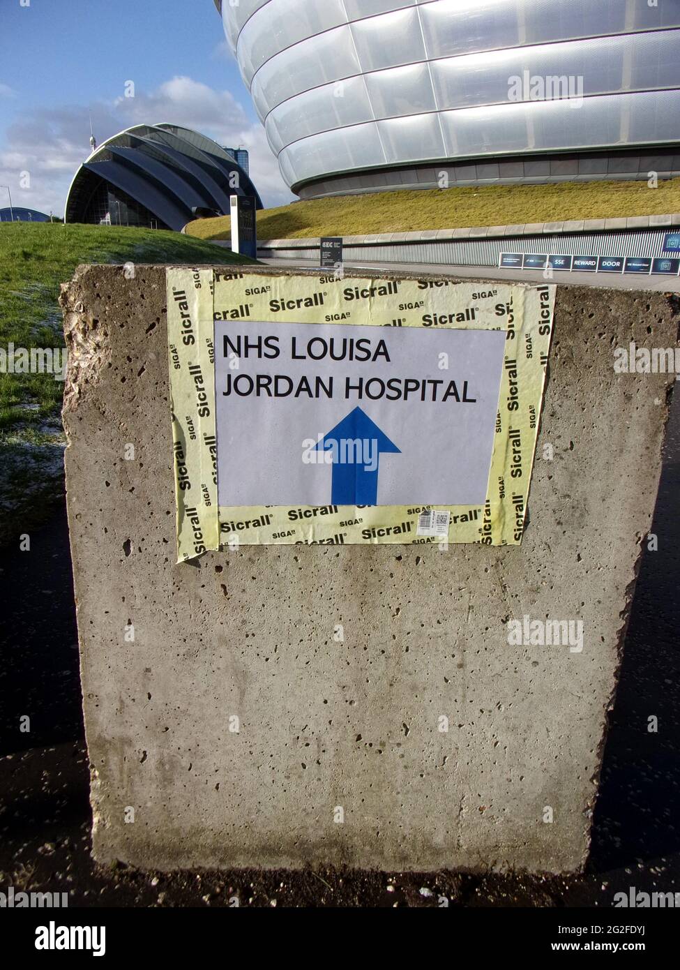 Ein Schild zeigt auf den riesigen Hydro Entertainment Complex in Glasgow. Das silberfarbene Äußere lässt ihn wie eine fliegende Untertasse aussehen und bietet Platz für 12,000 Personen. 2021 wurde es in ein NHS-Krankenhaus umgewandelt, in dem die Einwohner von Glasgow gegen das Covid-Virus geimpft werden konnten, das durch Großbritannien wütete. ALAN WYLIE/ALAMY© Stockfoto