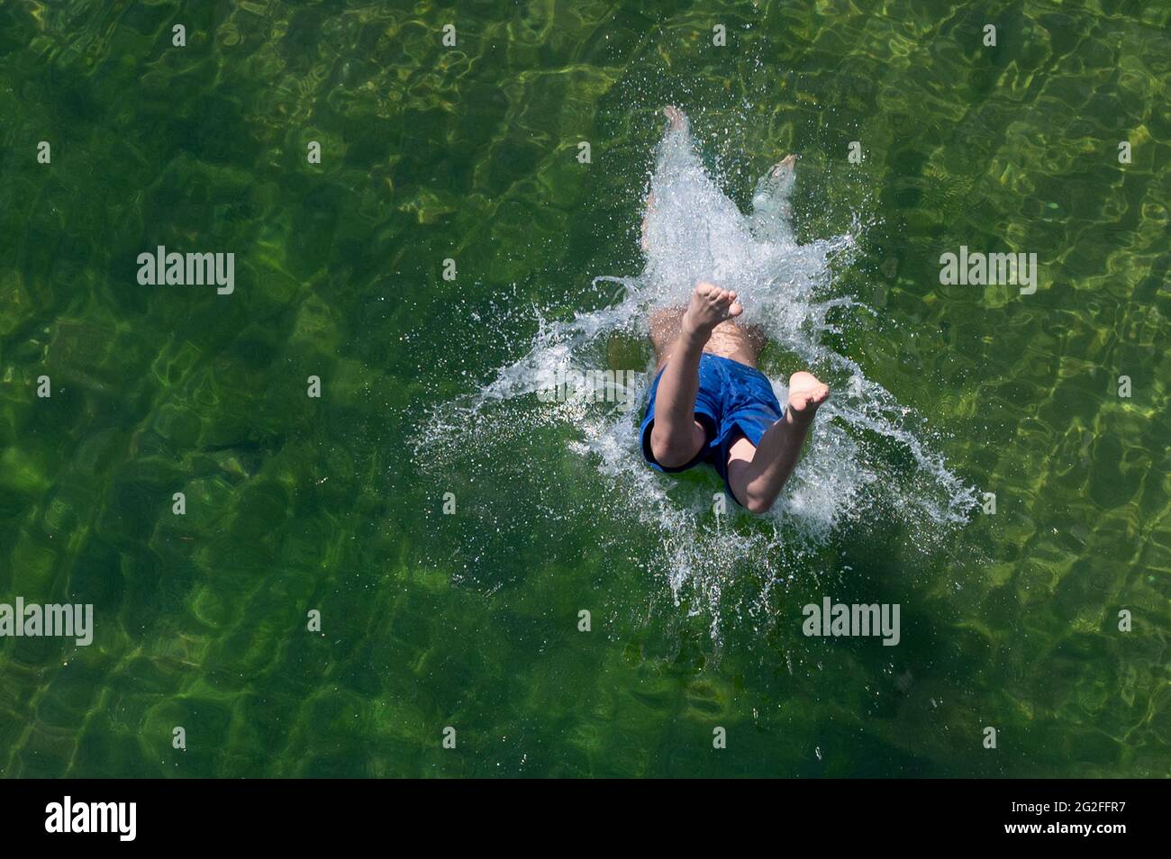 Dresden, Deutschland. Juni 2021. Ein Junge springt von einer hölzernen Fußgängerbrücke im Naturschwimmbad Mockritz ins Wasser. Die Freiluft-Badesaison wurde aufgrund von Corona mit einer Verzögerung im Freistaat eröffnet. Quelle: Sebastian Kahnert/dpa-Zentralbild/dpa/Alamy Live News Stockfoto