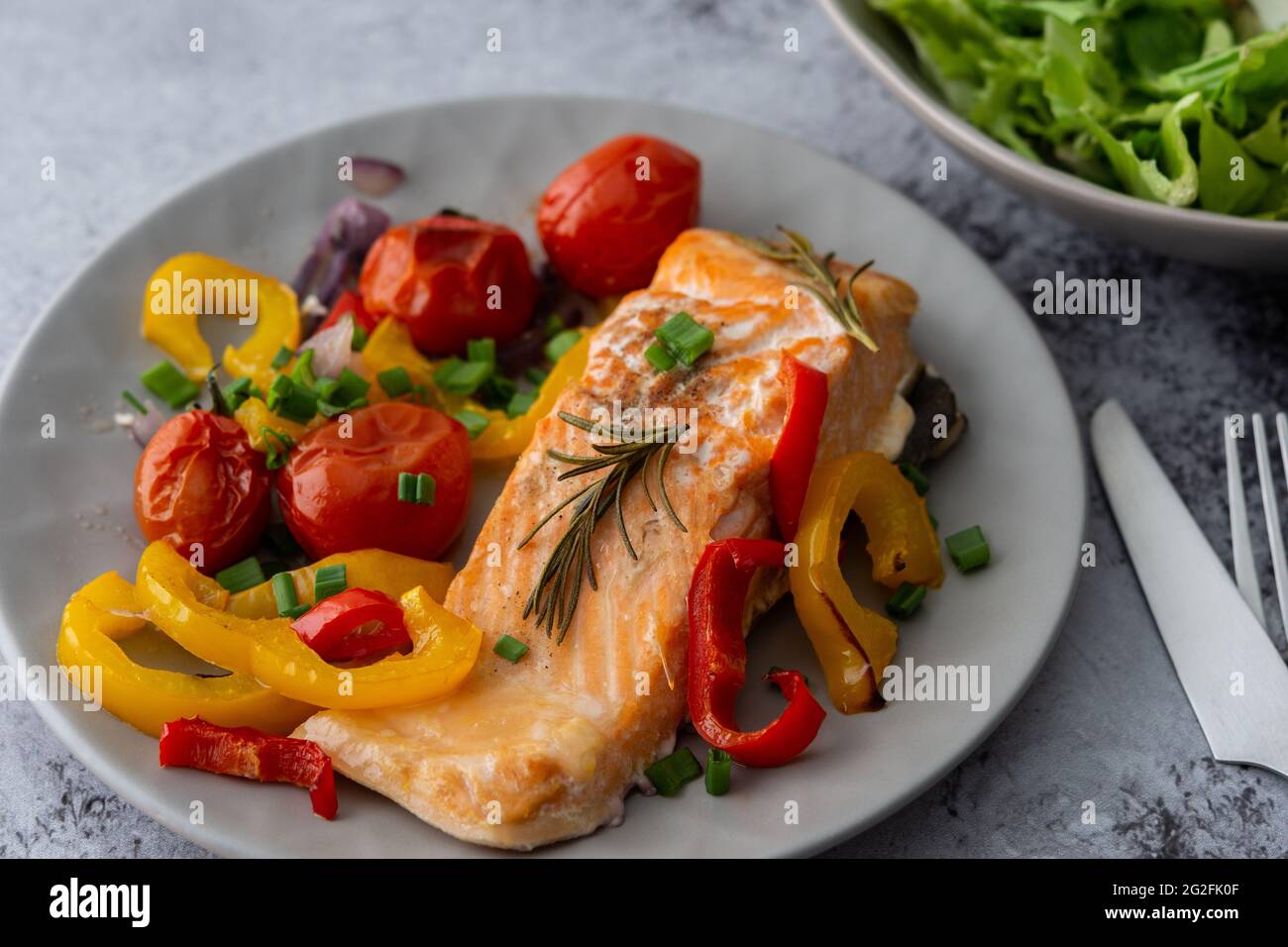 Gebackenes rotes Fischfilet Arctic Saibling auf einem Teller mit Gemüse, Salat in einer Schüssel mischen, leckeres herzhaftes gesundes Abendessen Stockfoto