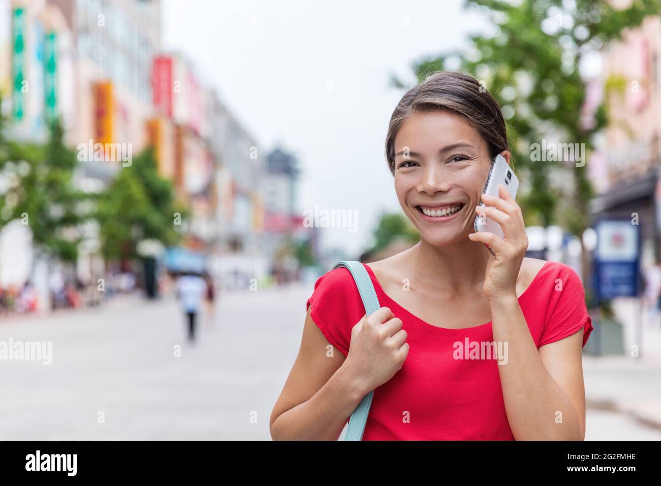 Chinesische Frau, die am Telefon sprach, während sie auf der Einkaufsstraße Wangfujing in Peking ging. Smart casual Geschäftsfrau mit mobilen App draußen Stockfoto