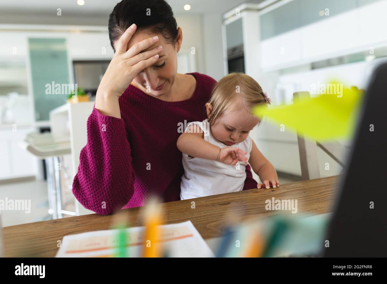 Gestresste kaukasische Mutter mit ihrem Baby, das ihren Kopf zu Hause hält Stockfoto