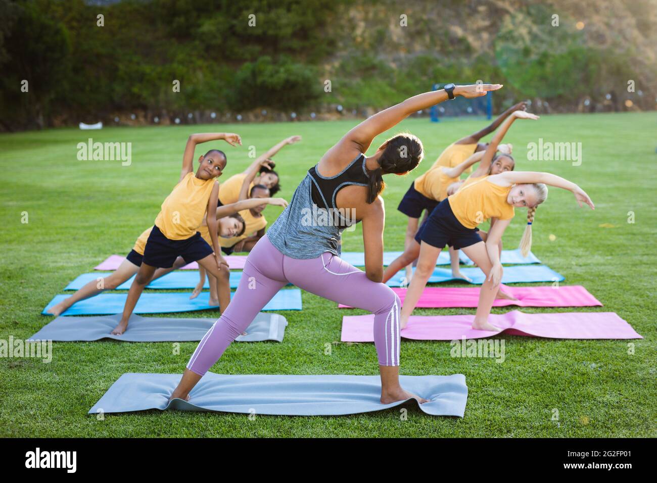 Lehrerin und eine Gruppe verschiedener Schüler, die im Garten der Schule Dehnübungen durchführen Stockfoto