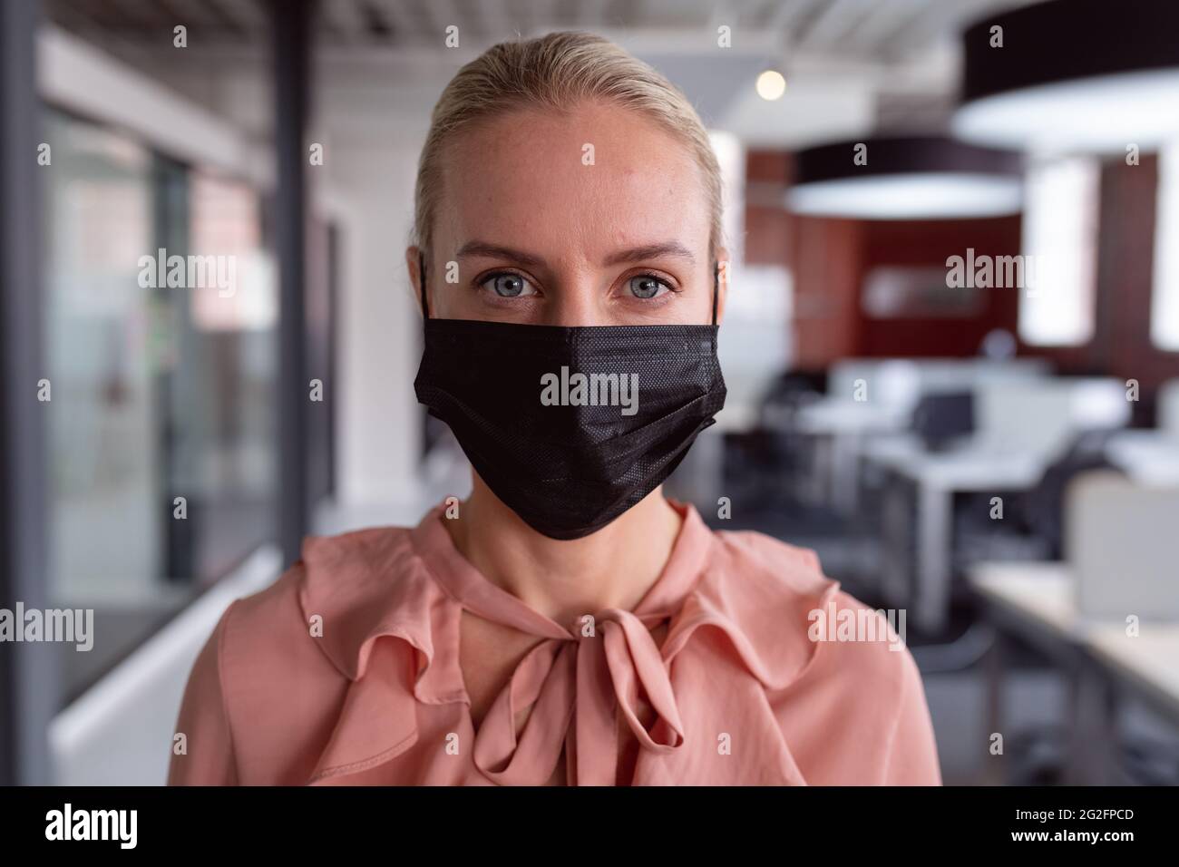 Porträt einer kaukasischen Geschäftsfrau mit Gesichtsmaske, die im Büro steht und vor die Kamera schaut Stockfoto