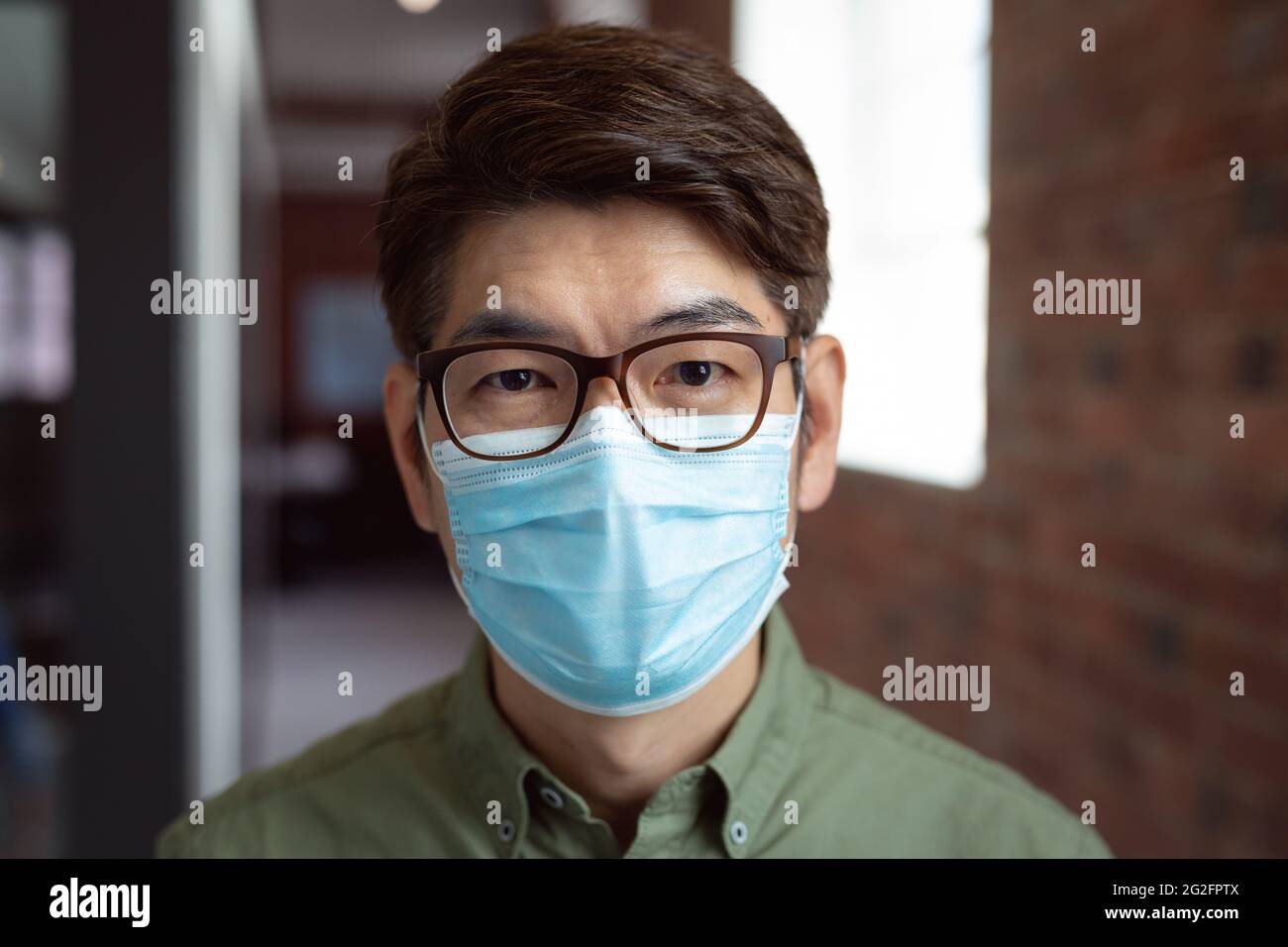 Porträt eines asiatischen Geschäftsmannes mit Gesichtsmaske im Büro mit Blick auf die Kamera Stockfoto