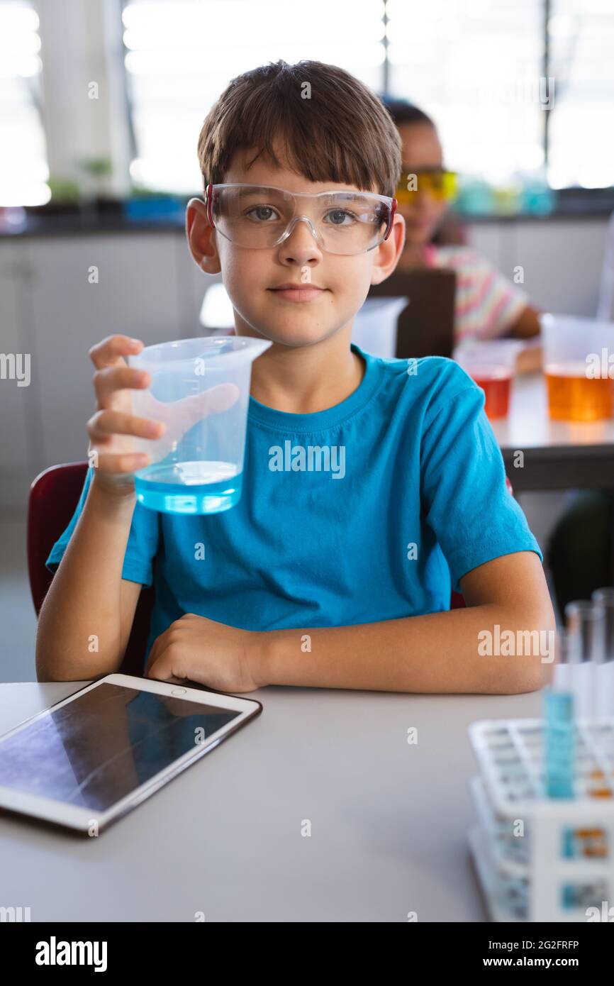 Porträt eines kaukasischen Jungen, der einen mit Chemikalien gefüllten Becher in der wissenschaftlichen Klasse im Labor hält Stockfoto