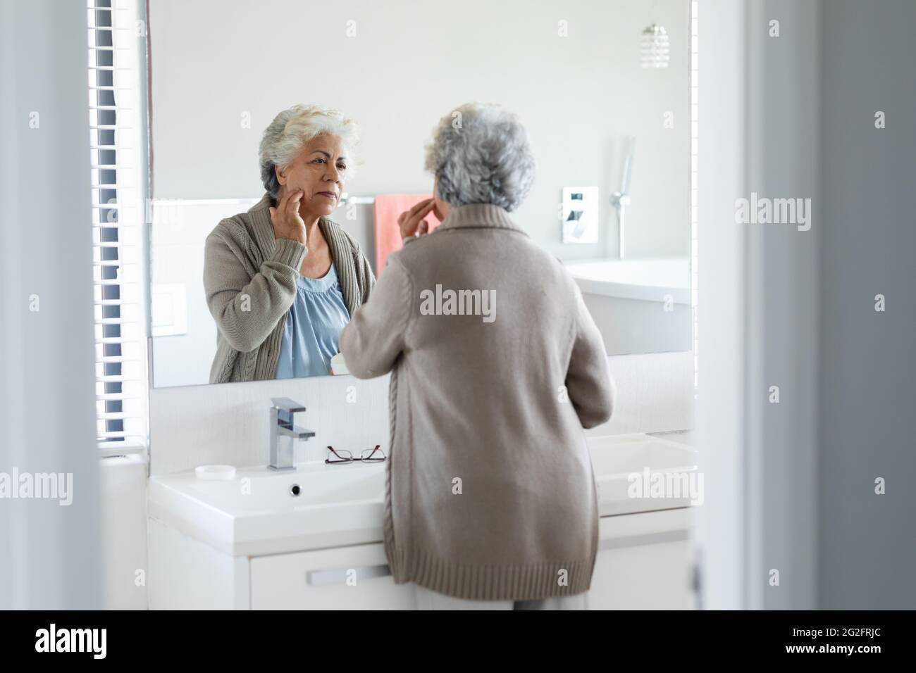 Ältere Frau mit gemischter Rasse, die ihre Spiegelung im Spiegel betrachtet Stockfoto