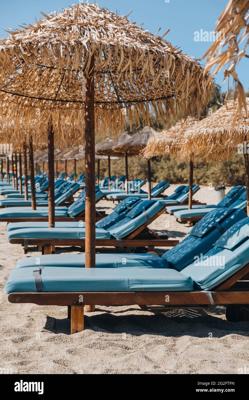 Eine Reihe von leeren blauen Sonnenliegen und Liegen unter den Sonnenschirmen an einem Strand in Mykonos, Griechenland. Stockfoto