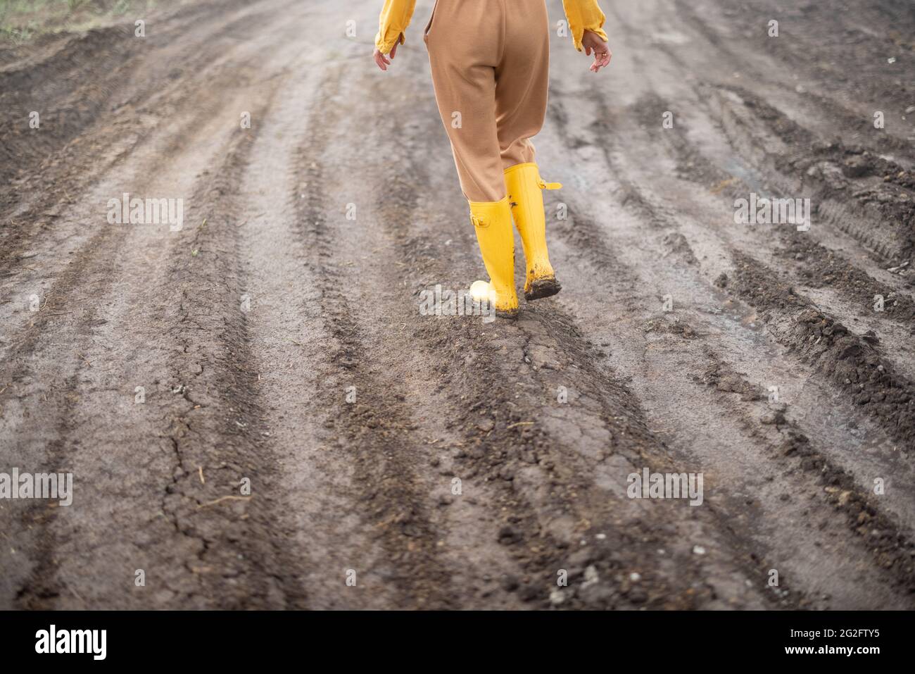 Beine einer Bäuerin in gelben Gummistiefeln, die nach dem Regen durch das kultivierte landwirtschaftliche Feld spazierend. Stockfoto