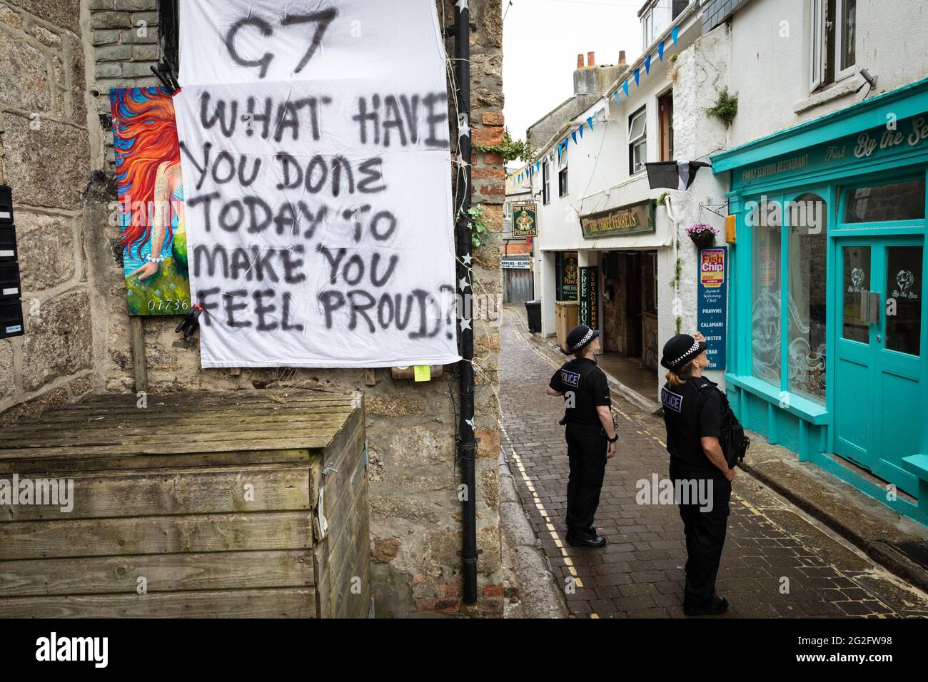 St Ives, Großbritannien. Juni 2021. Ein G7-Banner hängt in der Straße von St. Ives, während zwei Polizisten auf der Straße anhalten. Extinction Rebellion organisierte die Demonstration anlässlich des G7-Gipfels. Bei der Veranstaltung treffen sich die Staats- und Regierungschefs der Welt, um Fragen rund um den Klimawandel zu diskutieren. Kredit: Andy Barton/Alamy Live Nachrichten Stockfoto