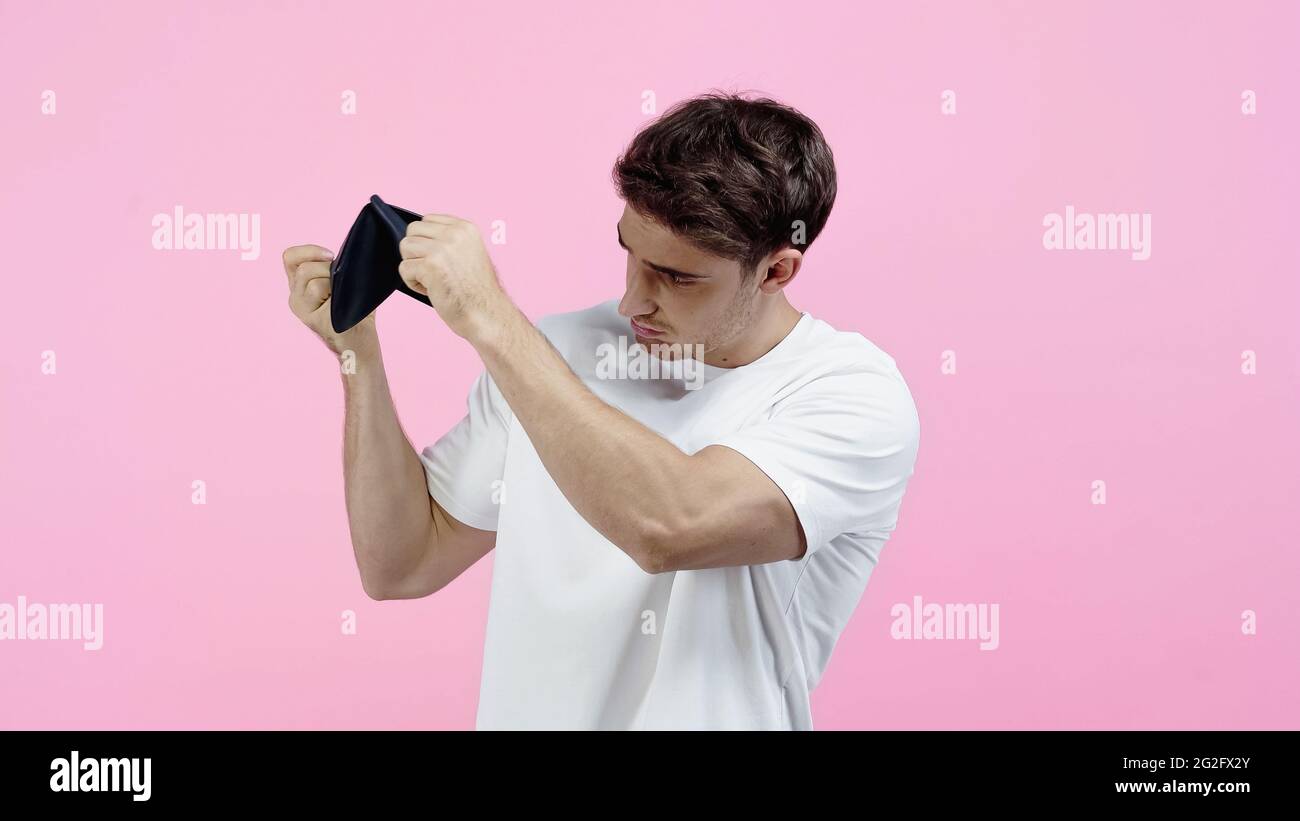 Junger Mann im weißen T-Shirt, der auf eine leere Brieftasche in Pink schaut Stockfoto