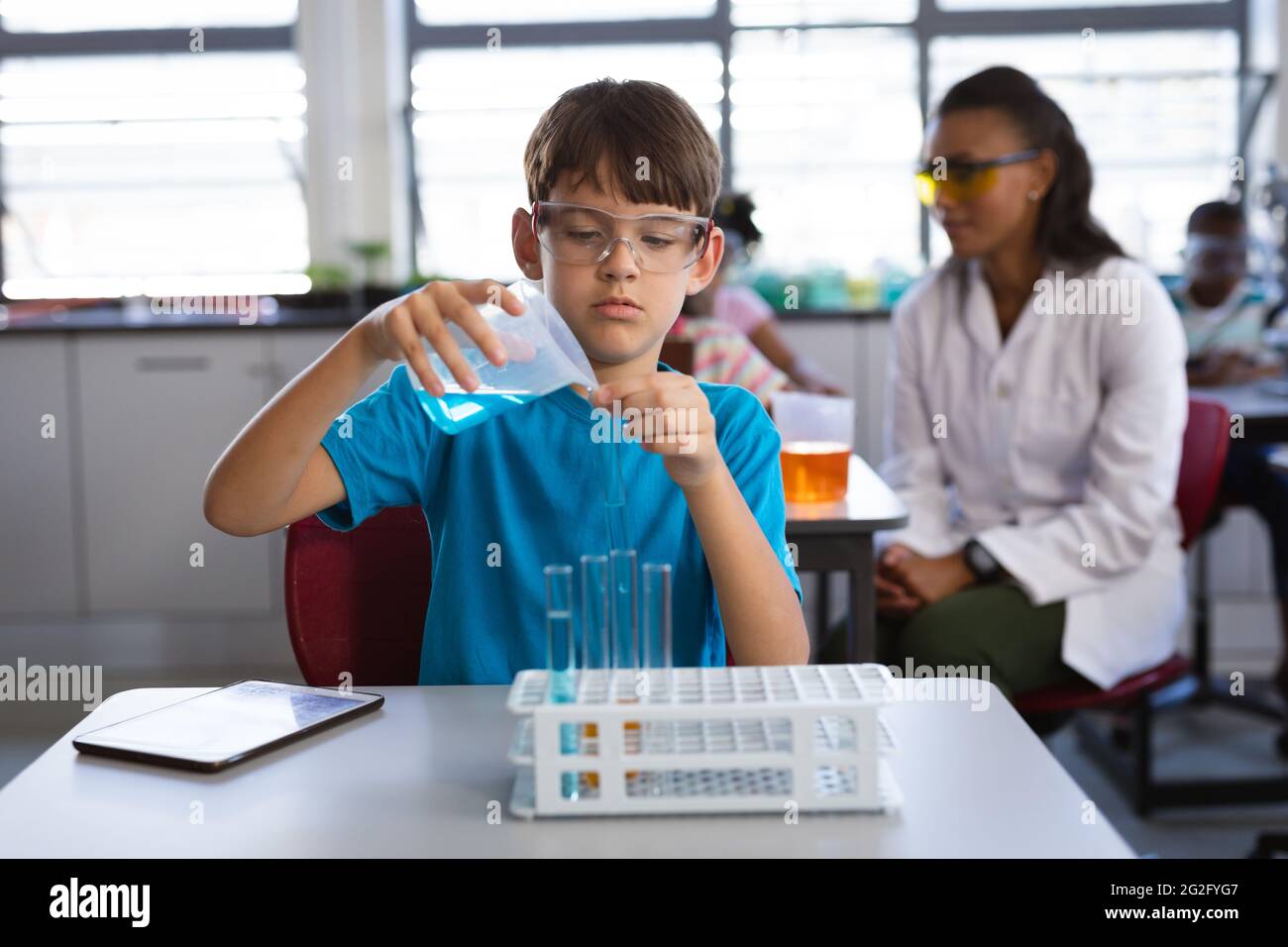 Kaukasischer Junge, der im wissenschaftlichen Unterricht im Labor Chemikalien aus dem Becher in das Reagenzglas gießt Stockfoto