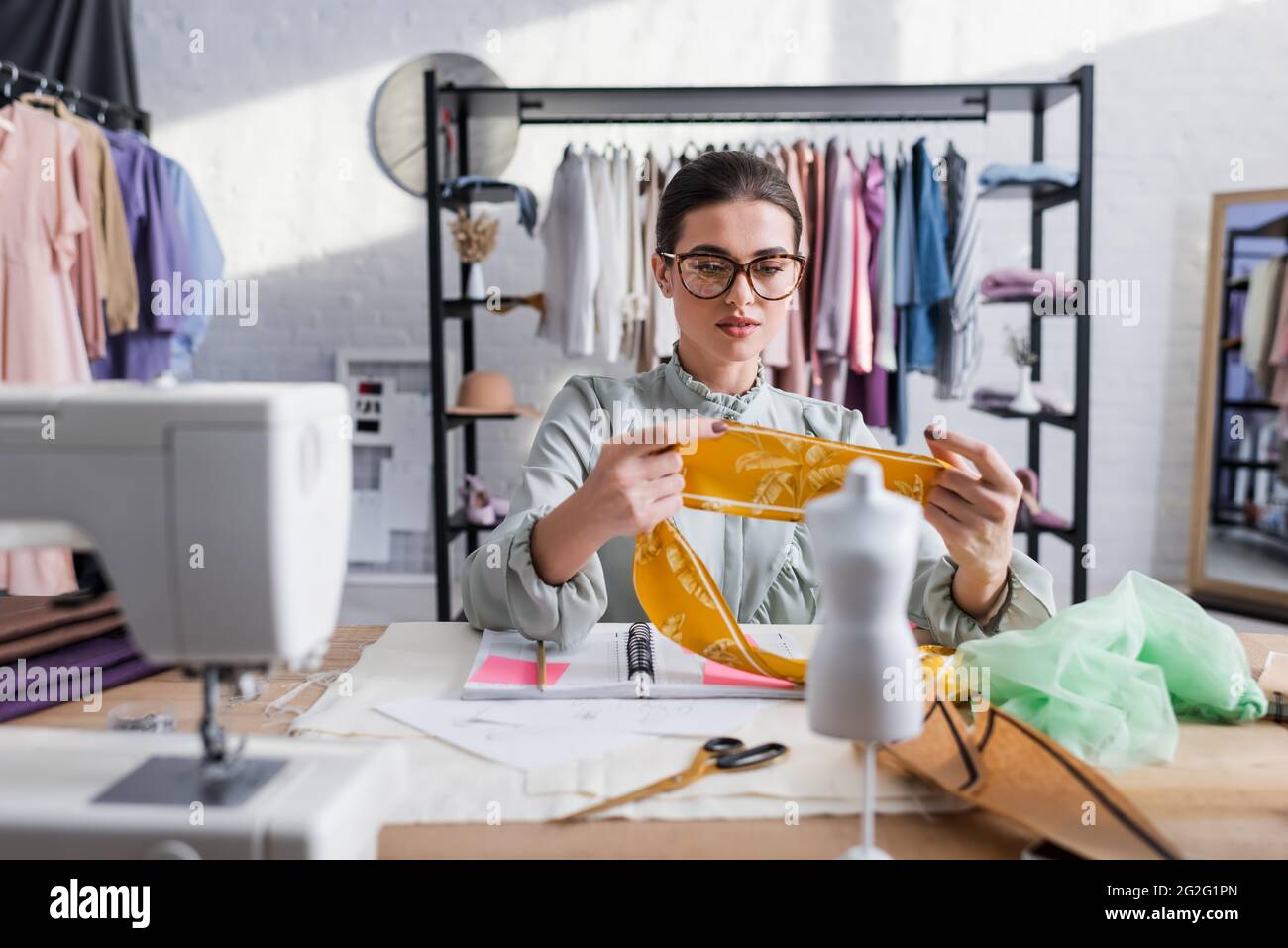 Näherin hält Tuch in der Nähe verschwommener Schaufensterpuppe und Nähmaschine Stockfoto