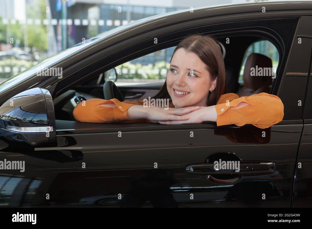 Fröhliche, schöne Frau, die fröhlich lächelt und in ihrem Auto sitzt Stockfoto