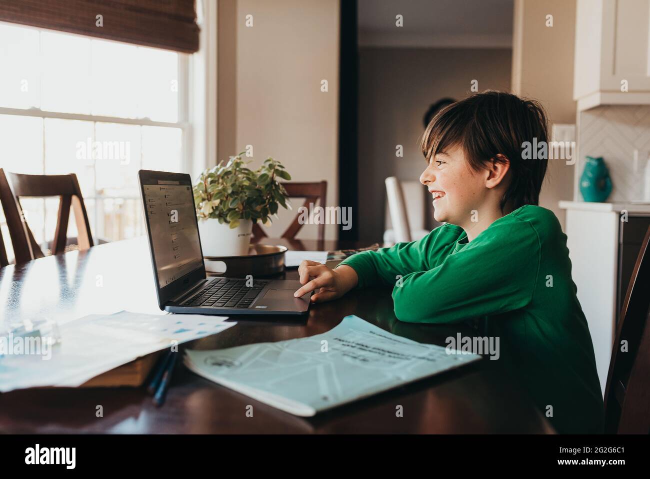 Glücklicher Junge, der auf der Schularbeit online am Computer am Küchentisch arbeitet. Stockfoto